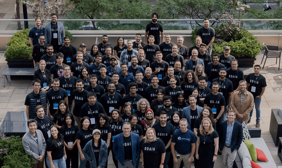 Large group of ODAIA team members posing outdoors, many wearing black ODAIA shirts and smiling.