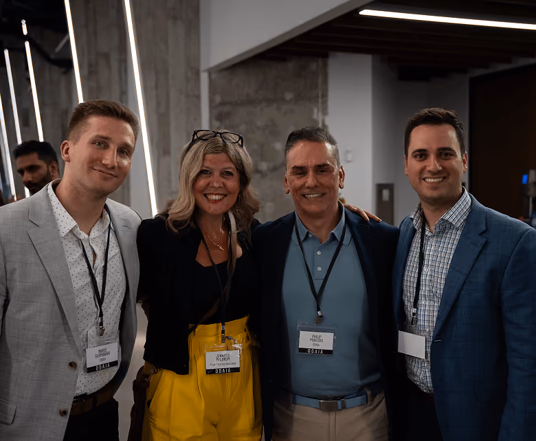 Group of four smiling adults with conference name badges standing together indoors.