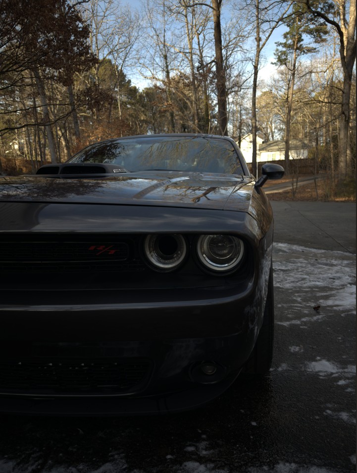 Front view of a black Dodge Challenger R/T parked on a driveway with trees and houses in the background.
