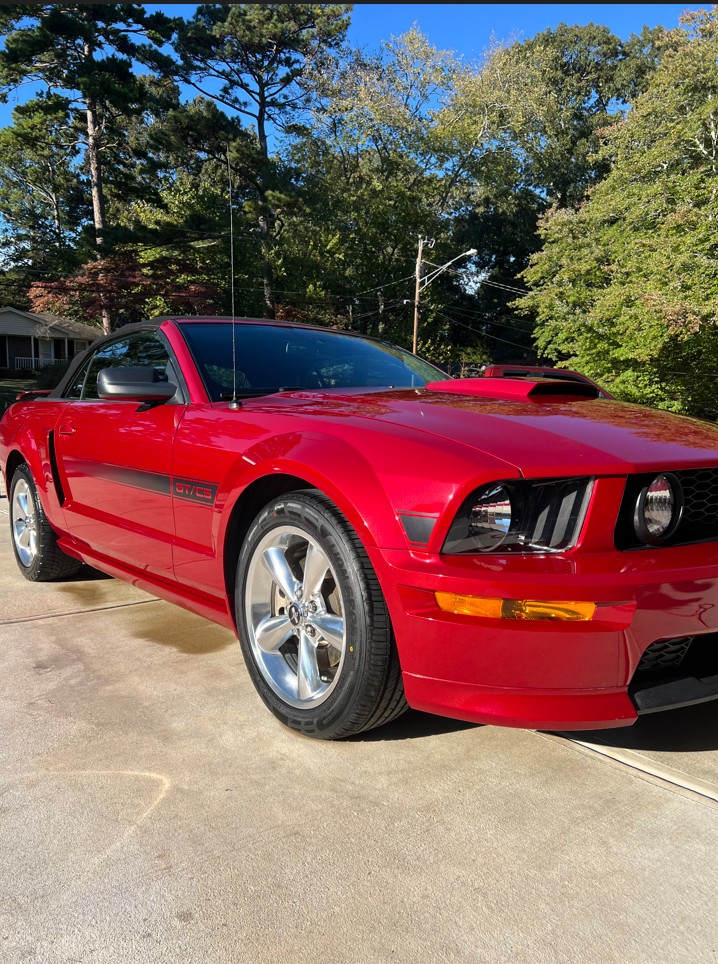 Red Ford Mustang GT/CS convertible parked on a driveway with trees in the background.