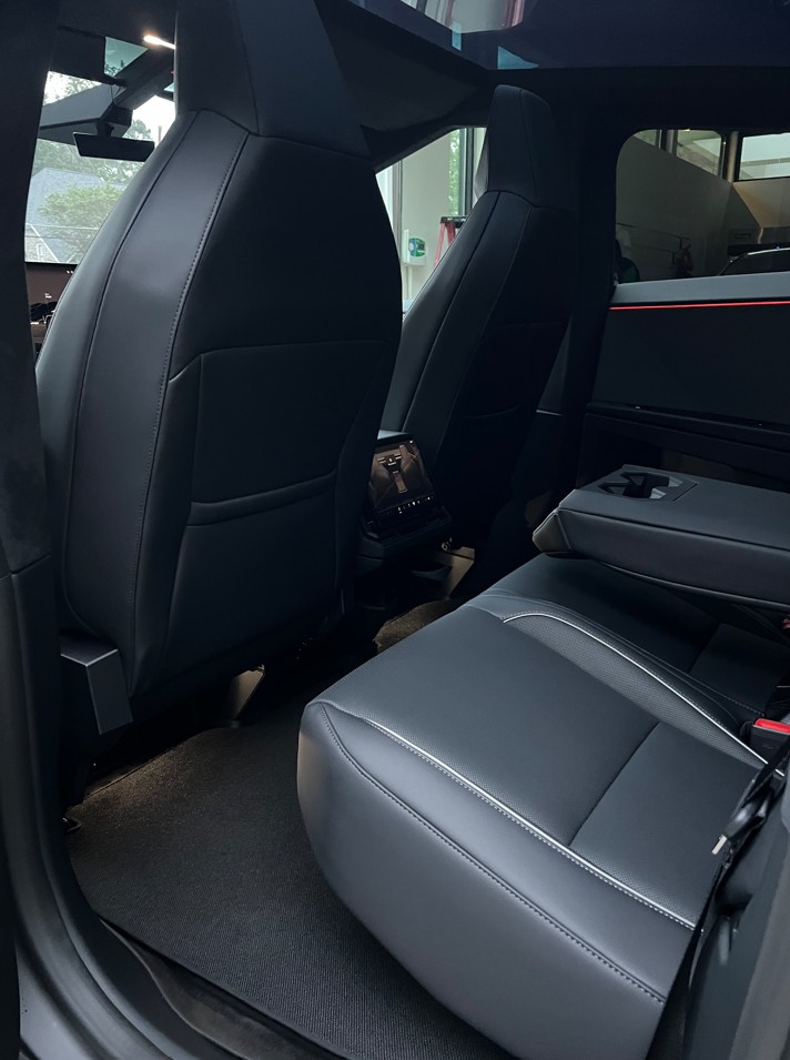 Rear interior view of a car showing the back of two black leather front seats and a black leather rear seat with an armrest and cup holders.