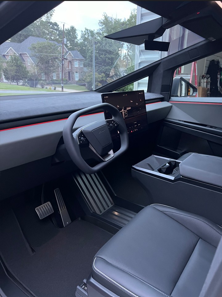 Interior of a modern electric vehicle showing a rectangular steering wheel, digital dashboard, large central touchscreen, and black leather seats.
