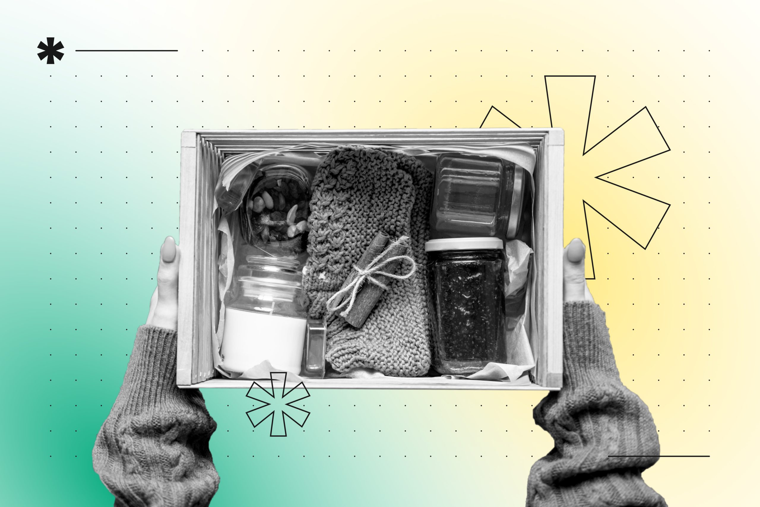 Hands holding a white subscription box filled with organized items including a knitted scarf, jars, headphones, and other cur