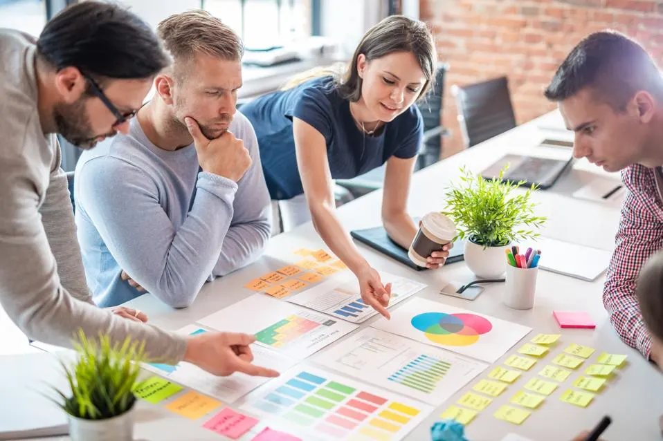 Team collaborating around a table with colorful charts, graphs, and sticky notes during a marketing strategy session