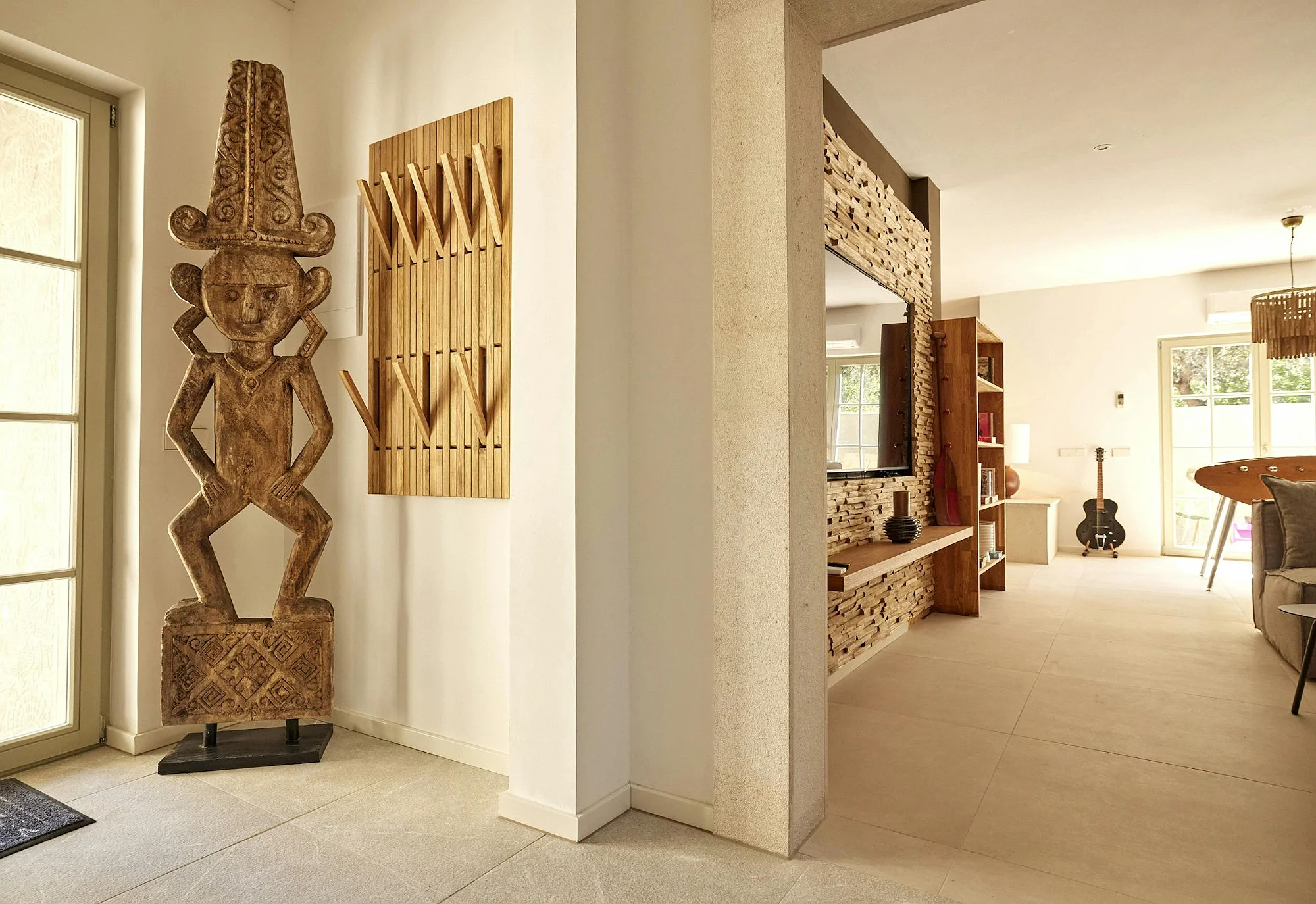 Entrance hall with ethnic wooden sculpture and view into living room at ByMilagro holiday villa Mallorca