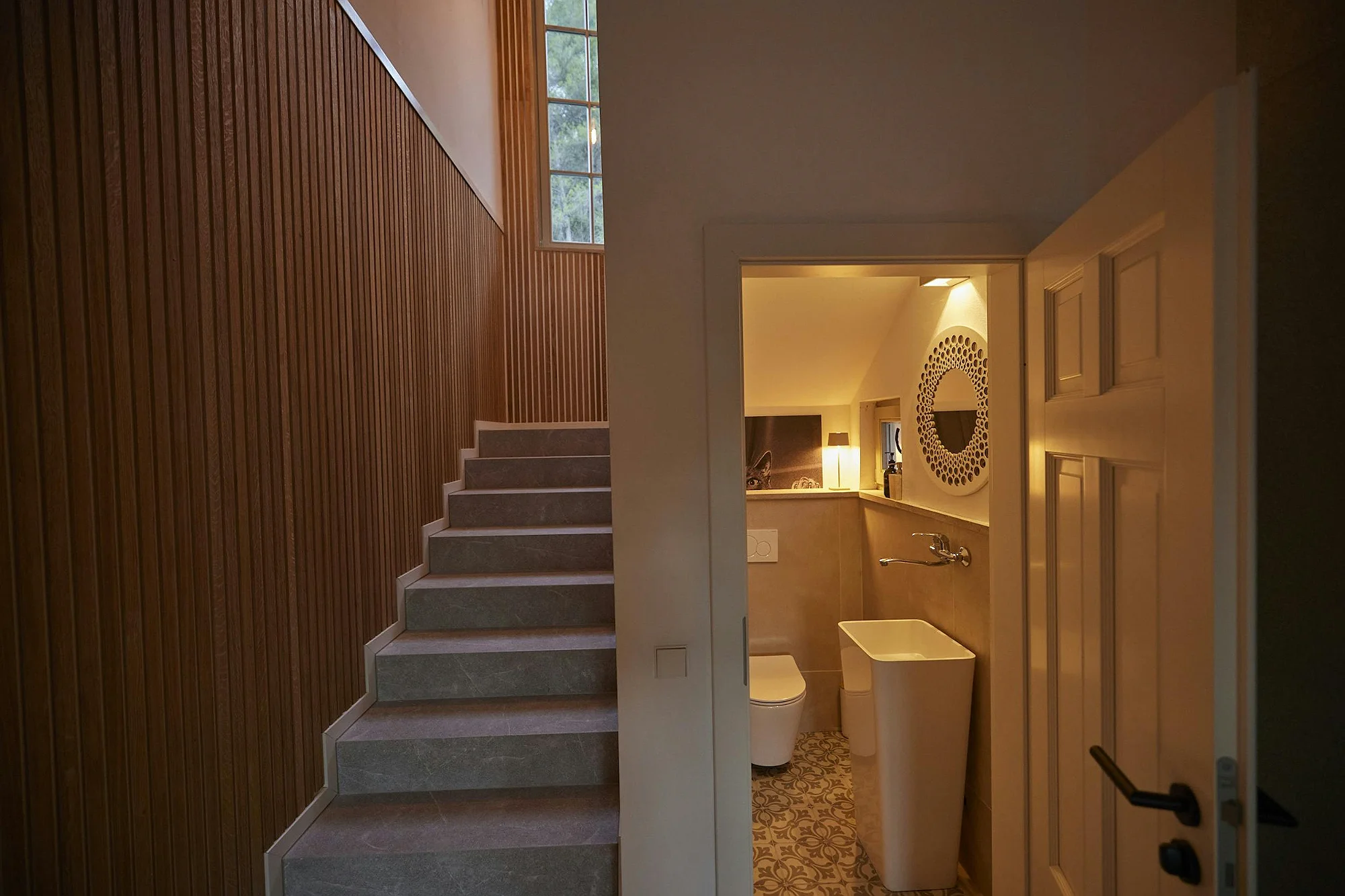 Modern staircase with wood paneling and stone steps, next to an elegant guest bathroom. ByMilagro luxury interior design.