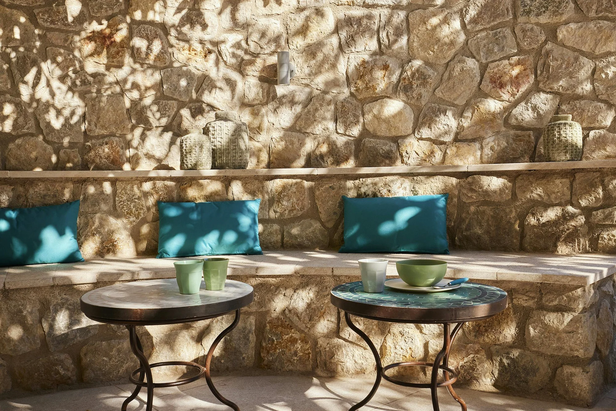 Outdoor lounge area with a stone wall, turquoise cushions, and marble tables. A relaxing corner at the ByMilagro luxury country home.