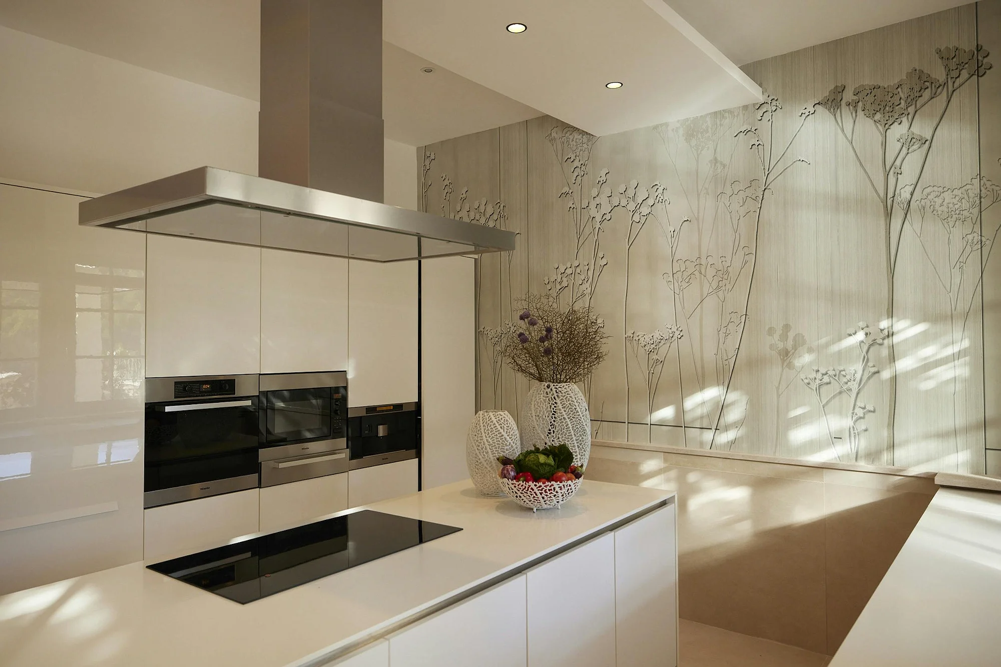 Modern high-gloss white kitchen with an island, integrated appliances, and a decorative wall with floral relief. ByMilagro exclusive property rentals.