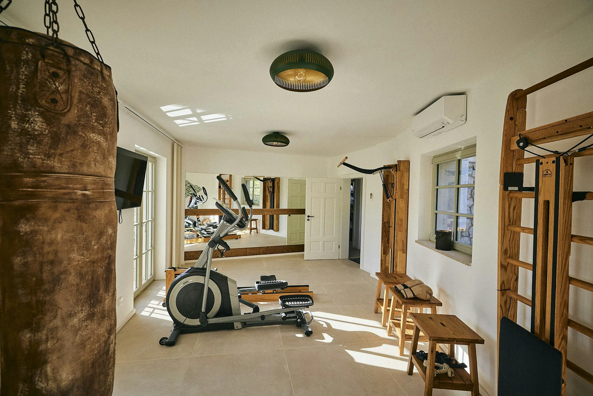Home gym with boxing bag, elliptical and wooden fitness equipment at ByMilagro luxury villa Mallorca