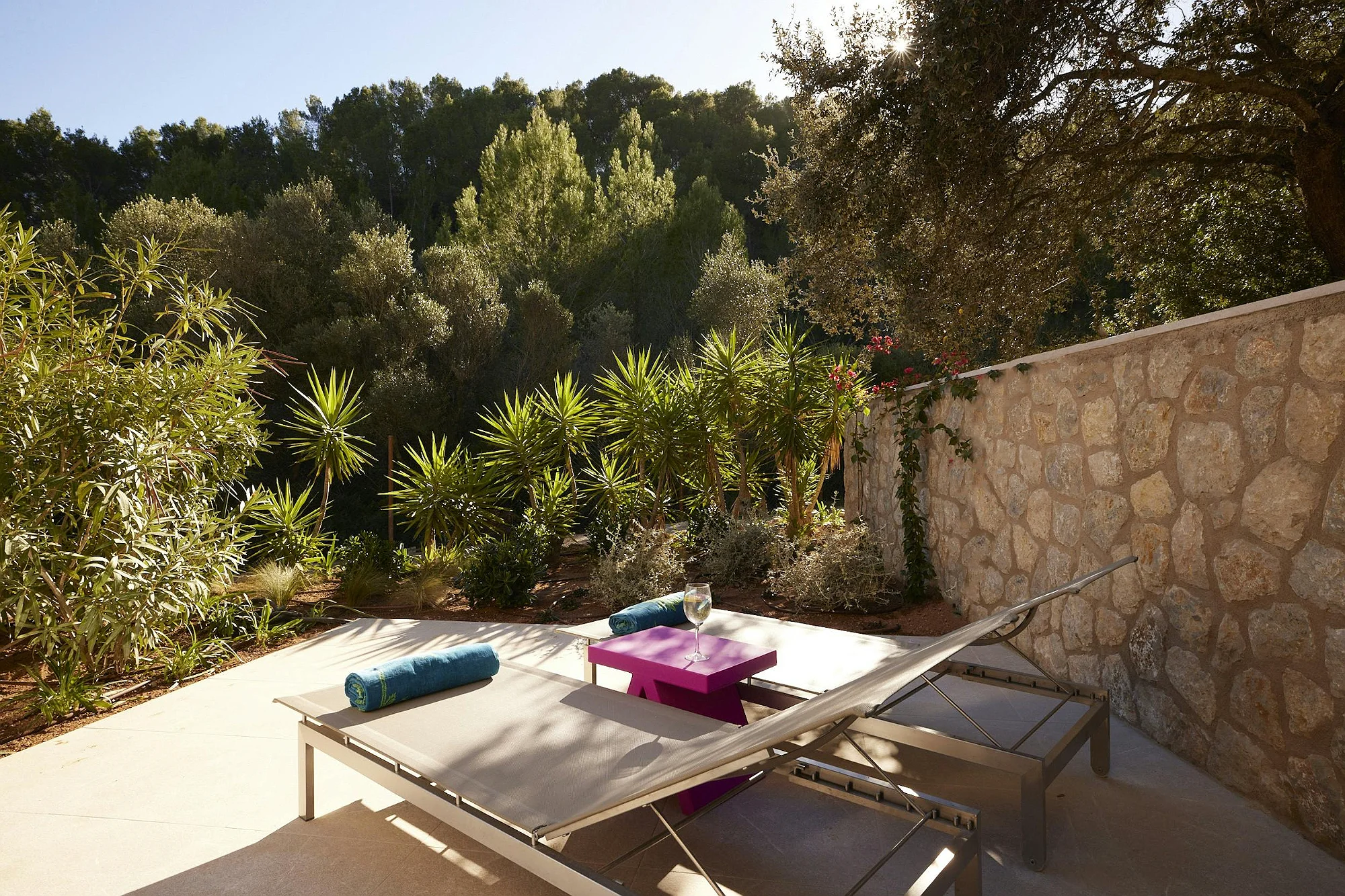Designer sun loungers with blue towels and a fuchsia side table in the solarium area. Mediterranean garden at the ByMilagro luxury rental villa.
