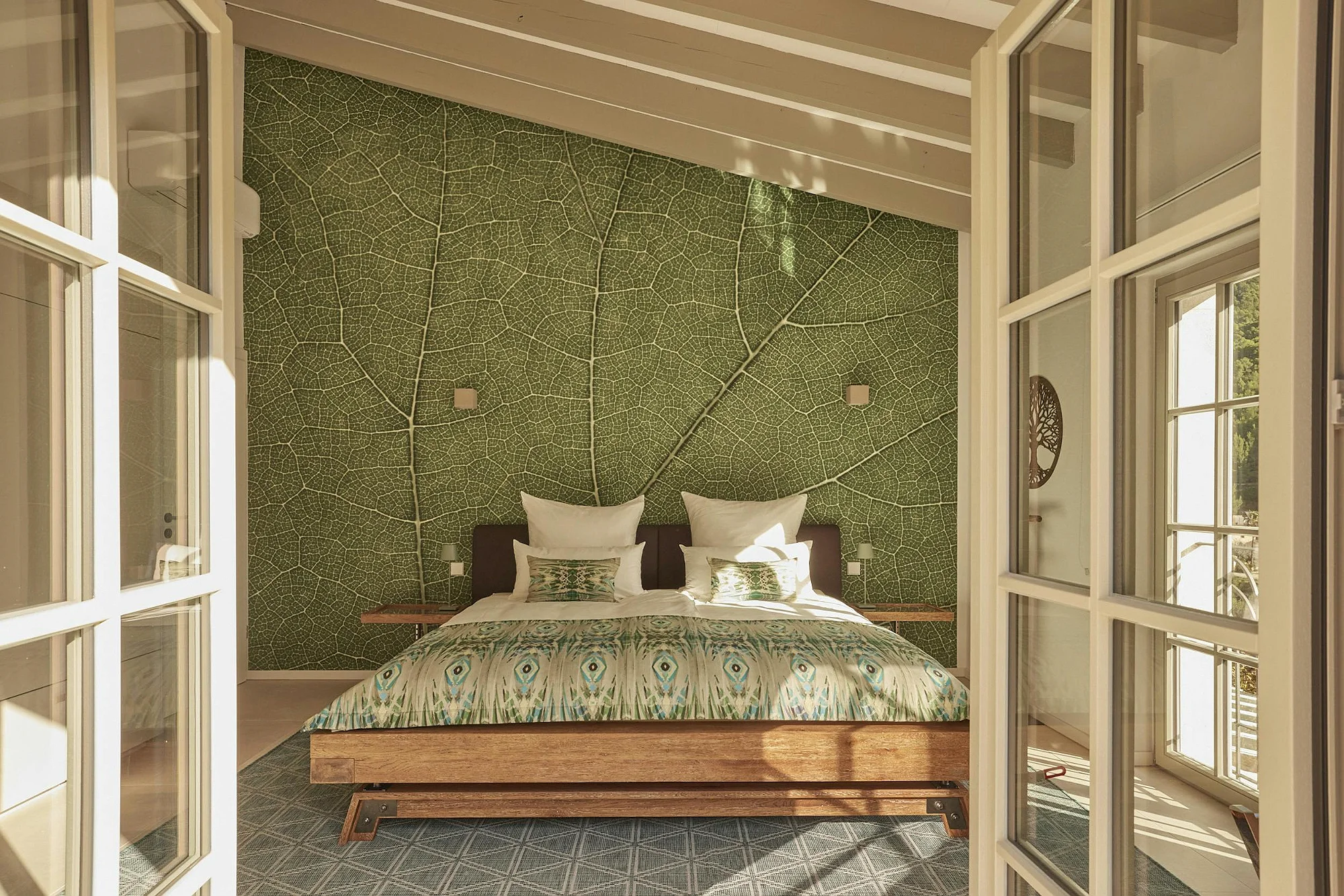 Boutique bedroom with floor-to-ceiling glass doors and a striking green leaf-pattern accent wall. Luxury vacation villa ByMilagro interior.