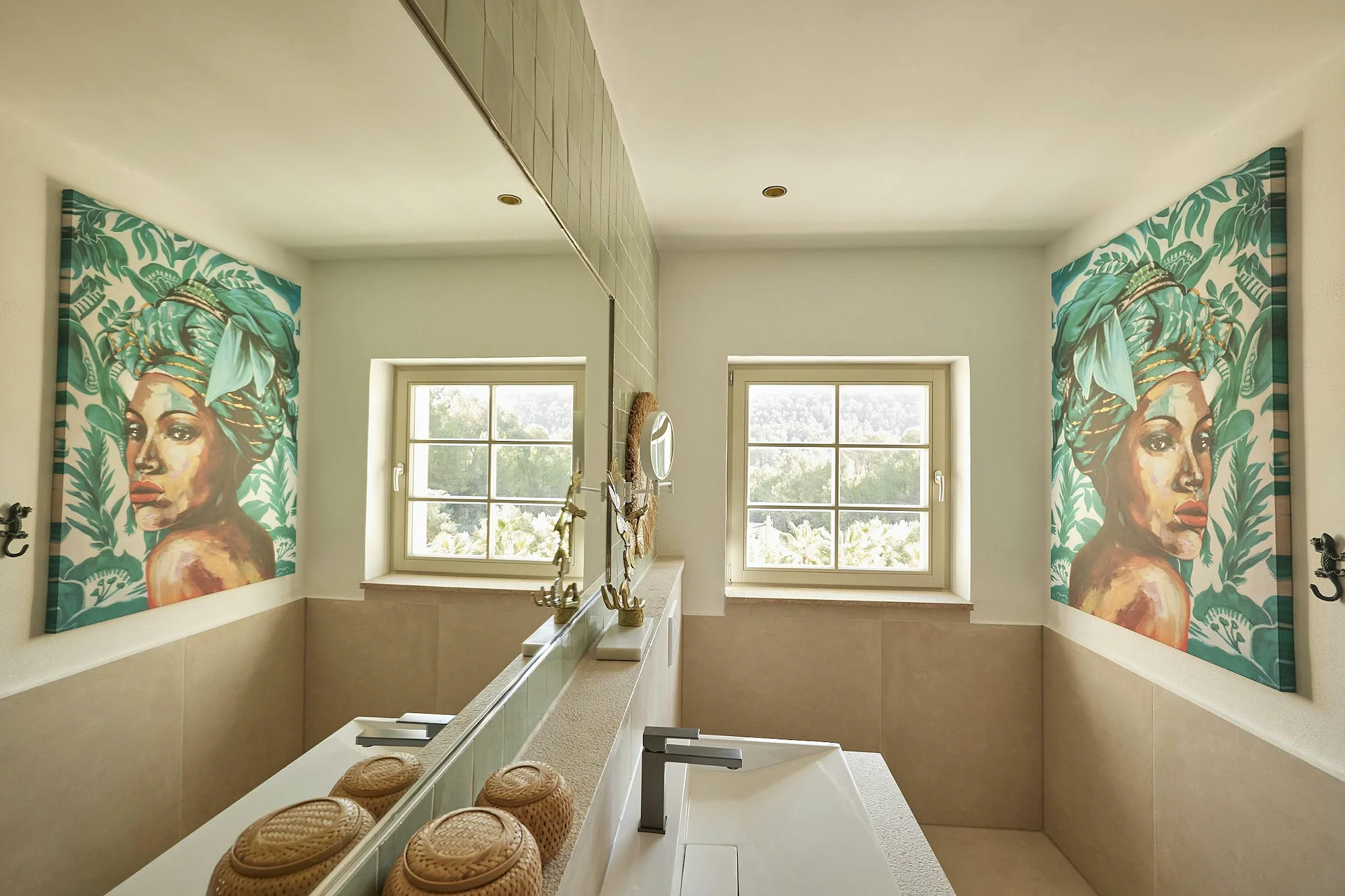 Designer bathroom with artistic wall canvas, large vanity mirror, and natural light from twin windows. Exclusive property rental ByMilagro decor.