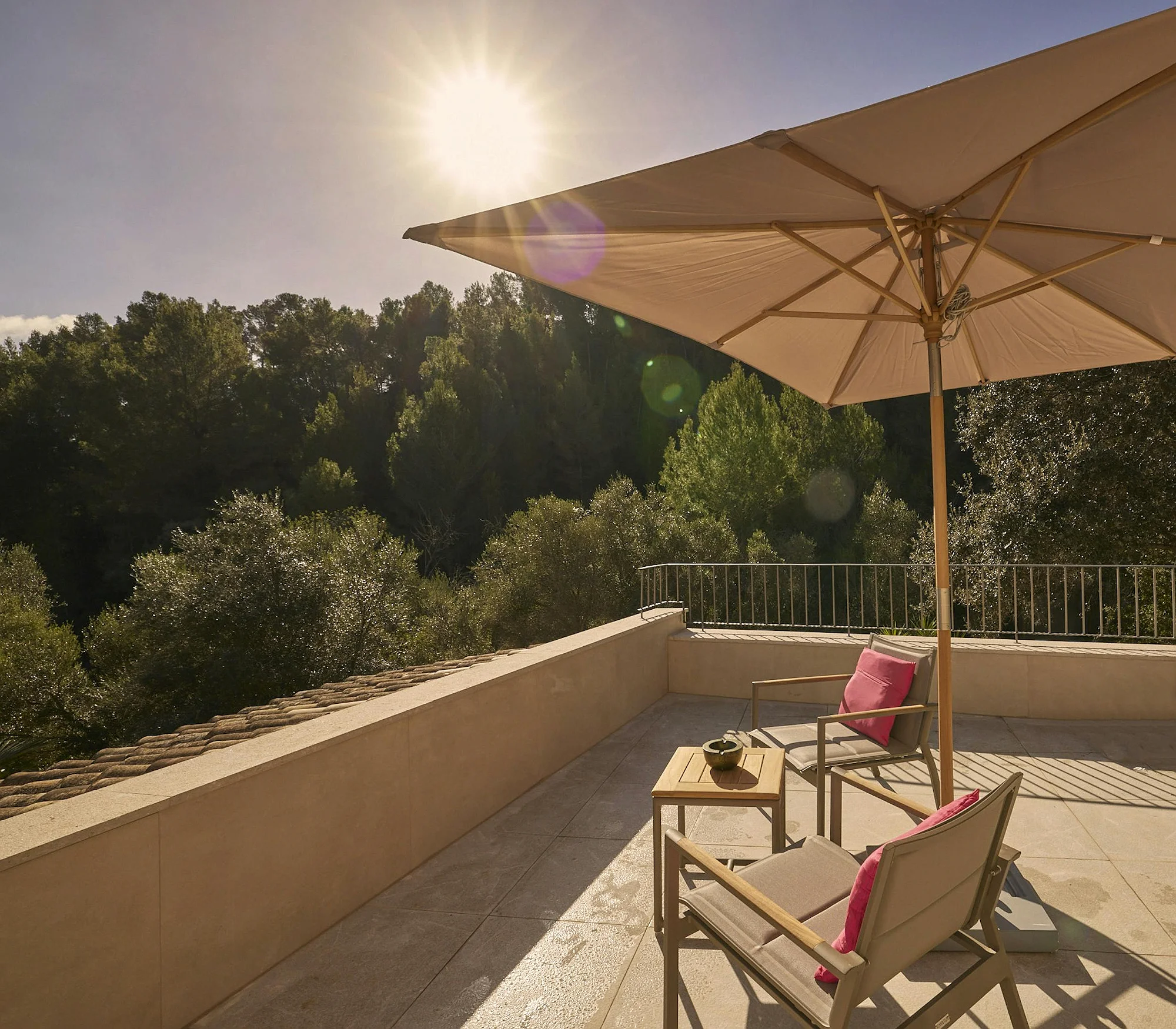 Sunny private terrace overlooking a forested landscape, with outdoor seating, parasol, and tiled flooring. ByMilagro luxury villa outdoor space.