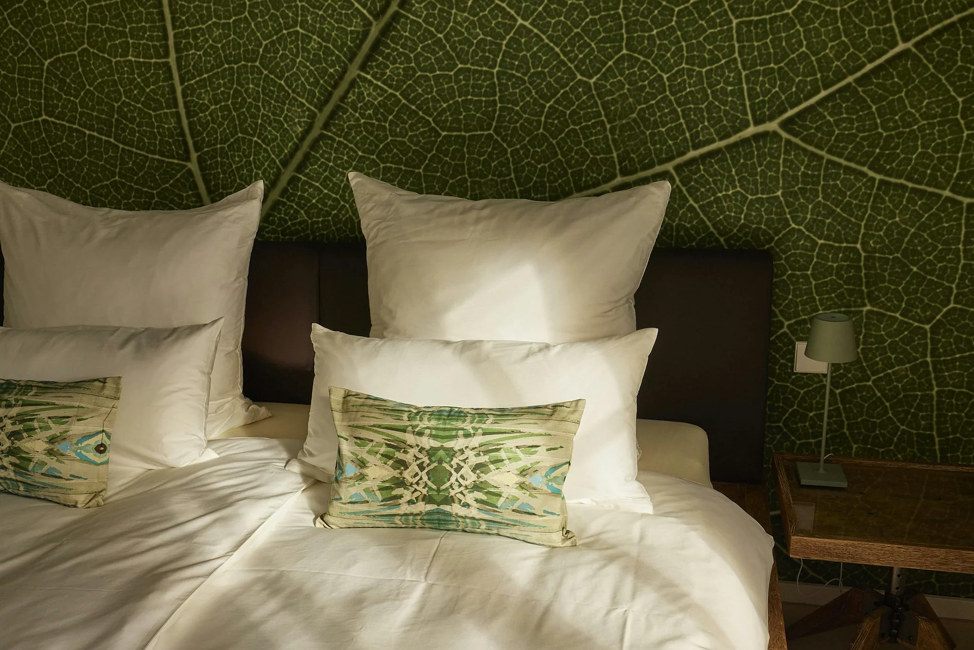 Close-up of the bed in the luxury ByMilagro property with crisp white linens and green-patterned pillows against the leaf-vein accent wall.