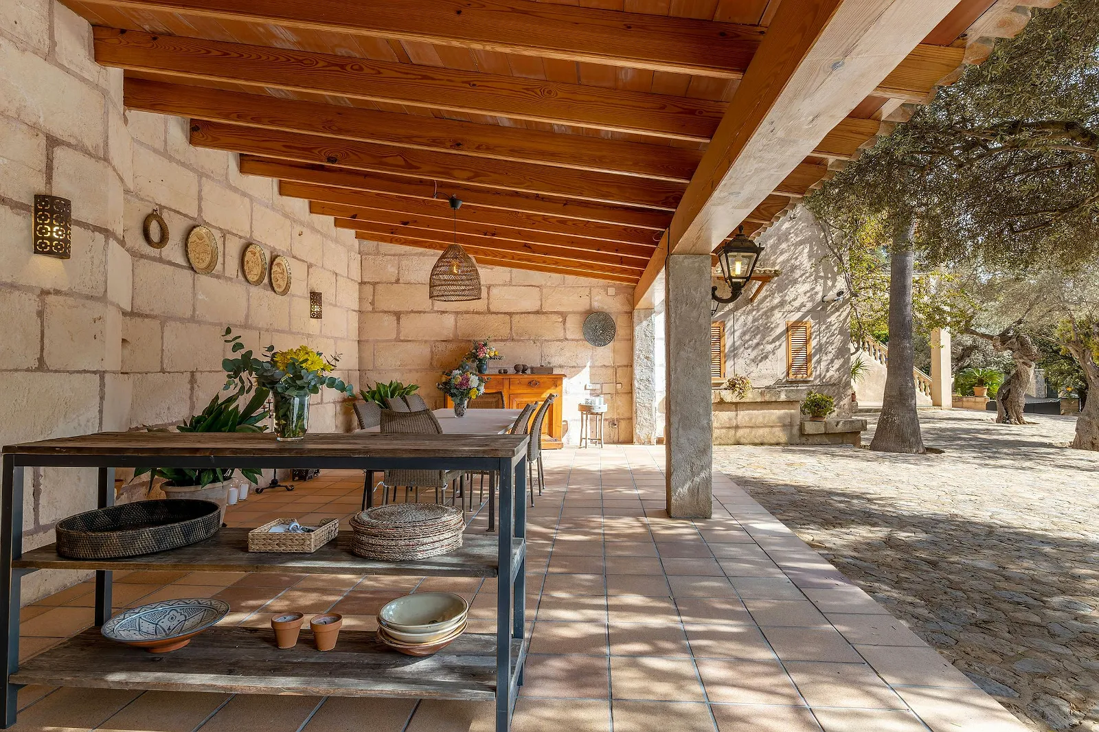 View of the spacious covered outdoor dining terrace at Villa Scarlett, showcasing the rustic stone facade and outdoor shelving unit. ByMilagro rental villa.