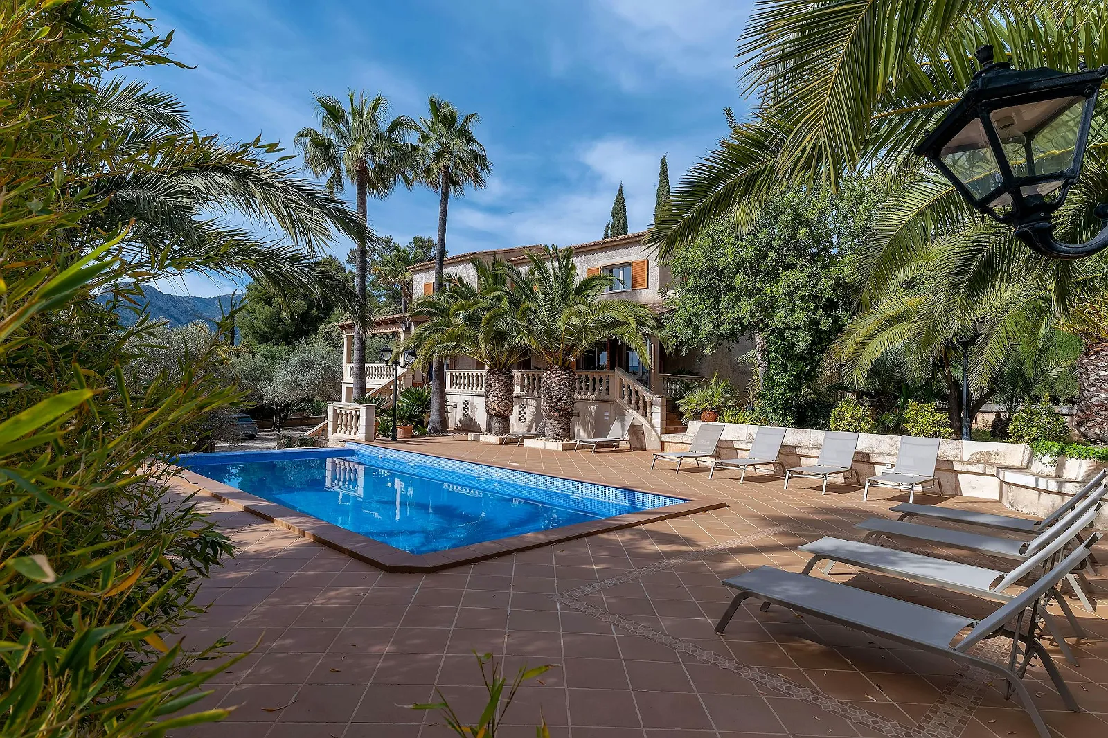 Stunning outdoor pool area at Villa Scarlett ByMilagro with tiled patio, lush tropical palm trees, and the main luxury villa in the background.