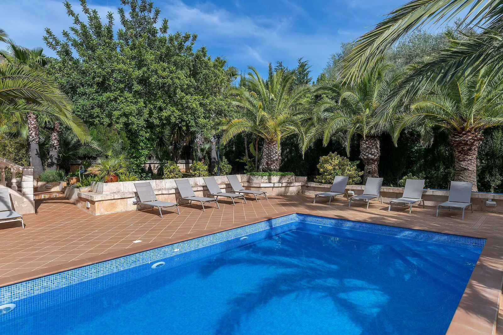 Close-up of the bright blue private swimming pool and sun deck with multiple grey sun loungers at Villa Scarlett luxury villa ByMilagro.