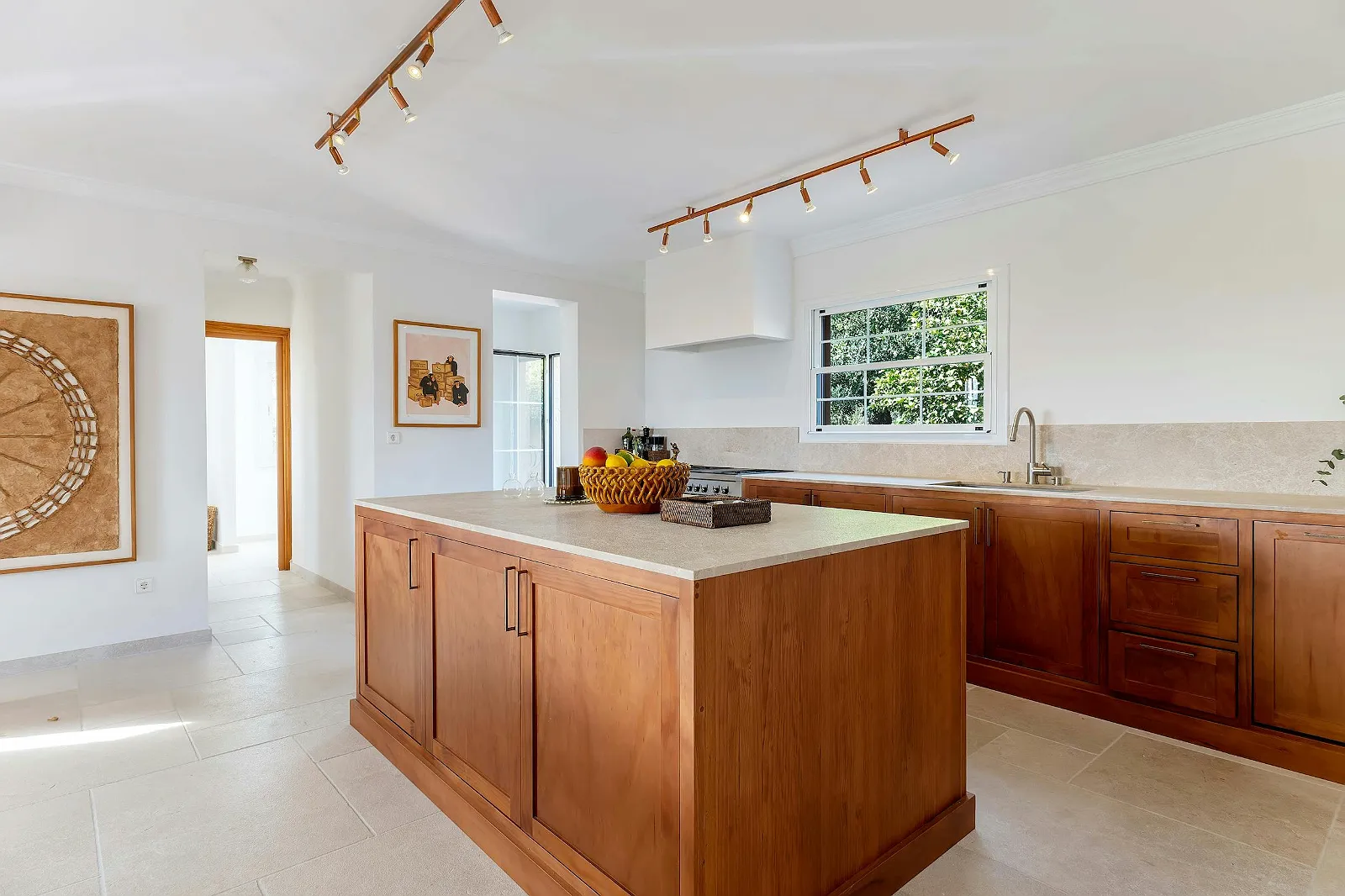 Villa Scarlett bright kitchen with central wooden island, track lighting, and stone countertops, offering a clean, rustic-modern feel. ByMilagro.