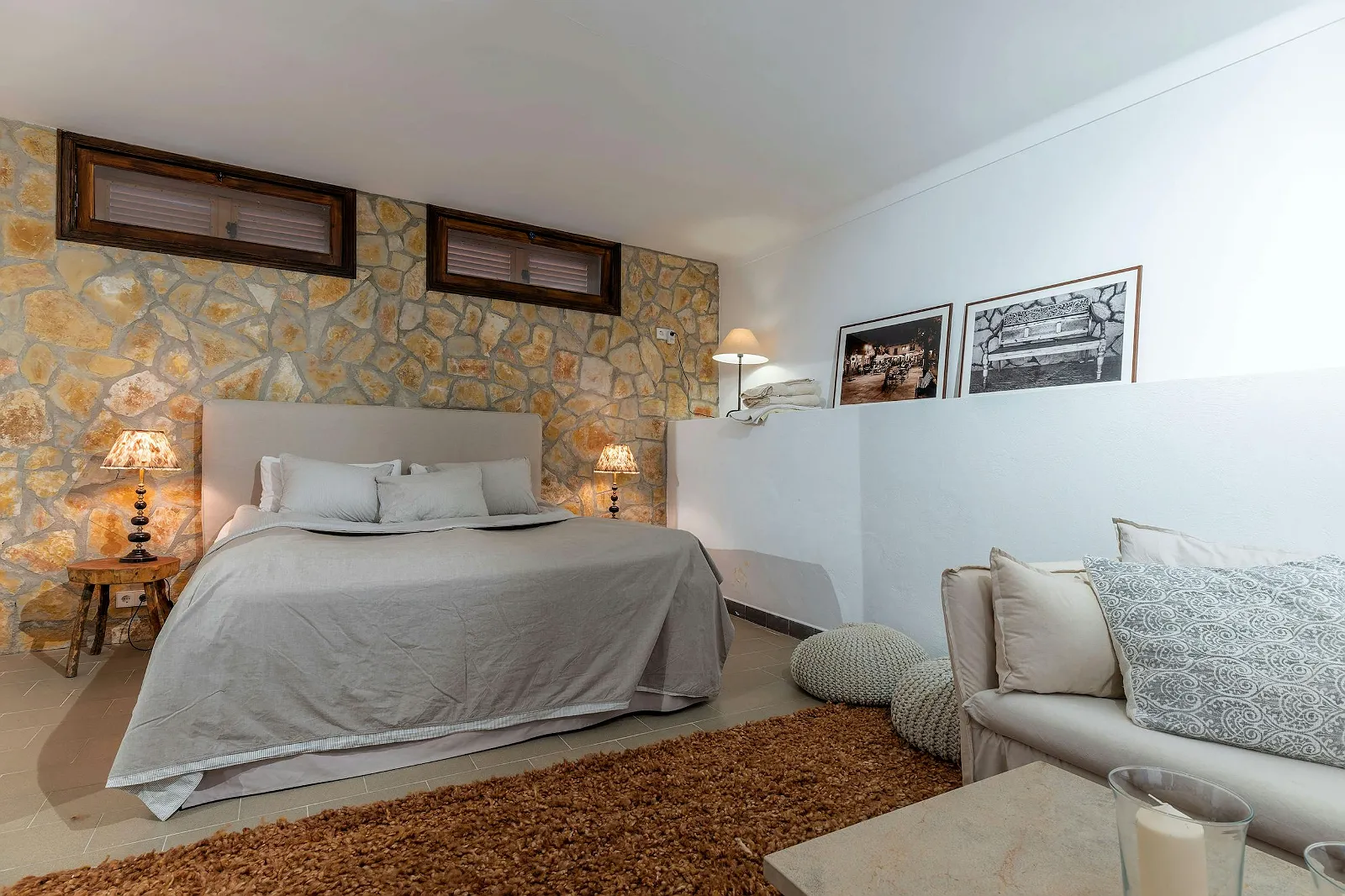 Comfortable guest bedroom in Villa Scarlett with natural stone wall, plush bed, side lamps, and small sitting area. Luxury accommodation ByMilagro.