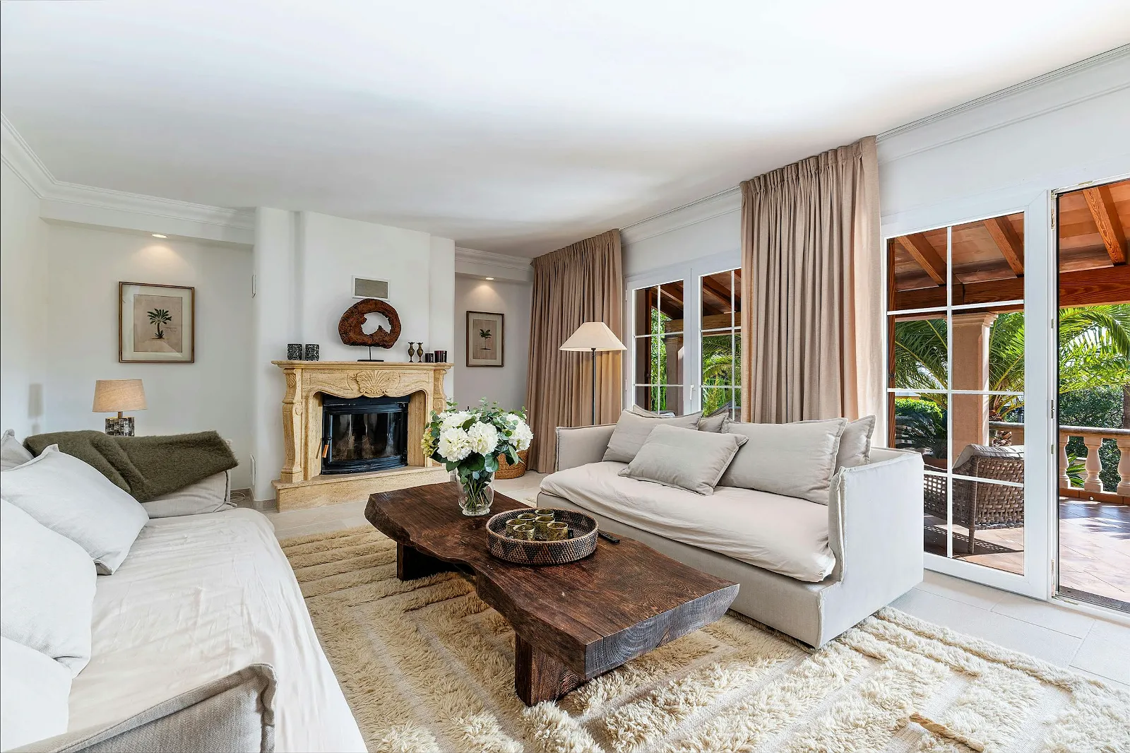Bright luxury living room in Villa Scarlett ByMilagro with stone fireplace, comfortable sofas, rustic wooden coffee table, and glass doors to the terrace.