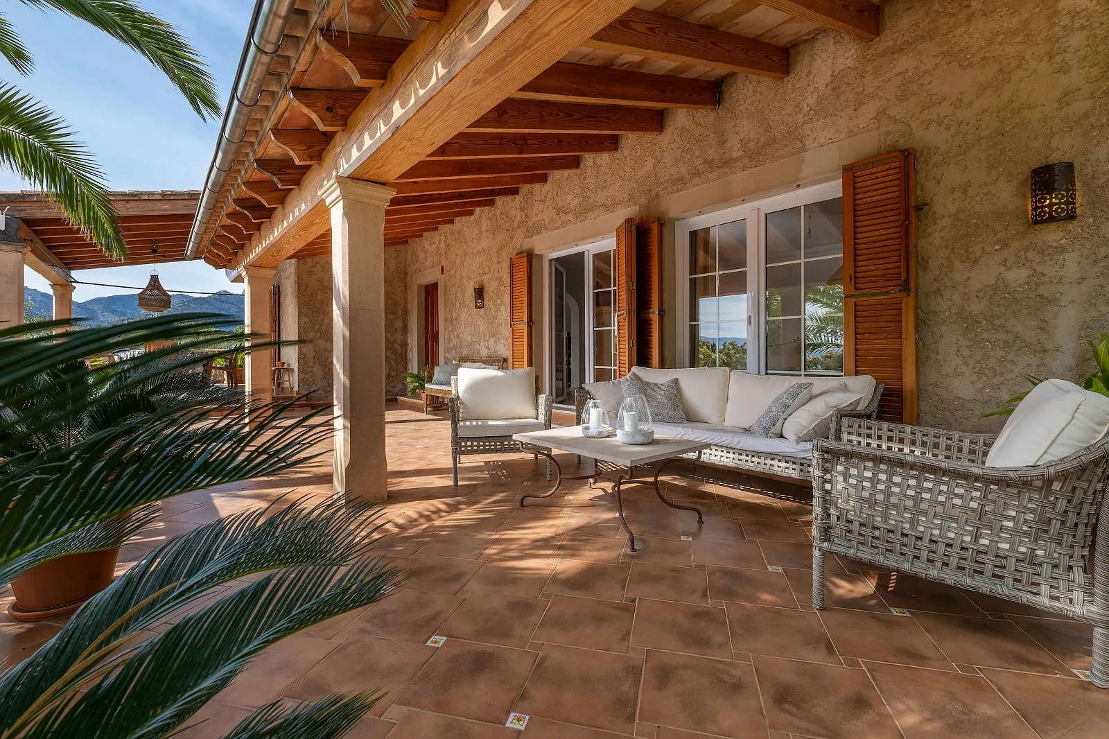 Shaded covered terrace at Villa Scarlett with outdoor sofa and chairs, terracotta tiles, and mountain views. Ideal luxury vacation rental feature.