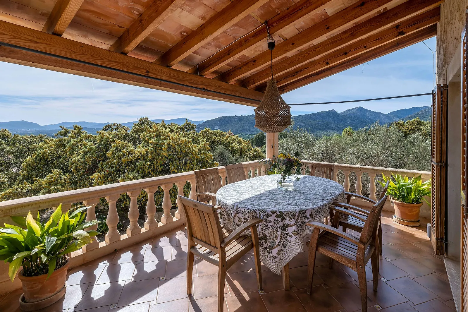 Terrace dining area on the upper level with stunning mountain views, wooden table and chairs, and a covered patio roof. Luxury villa ByMilagro balcony.