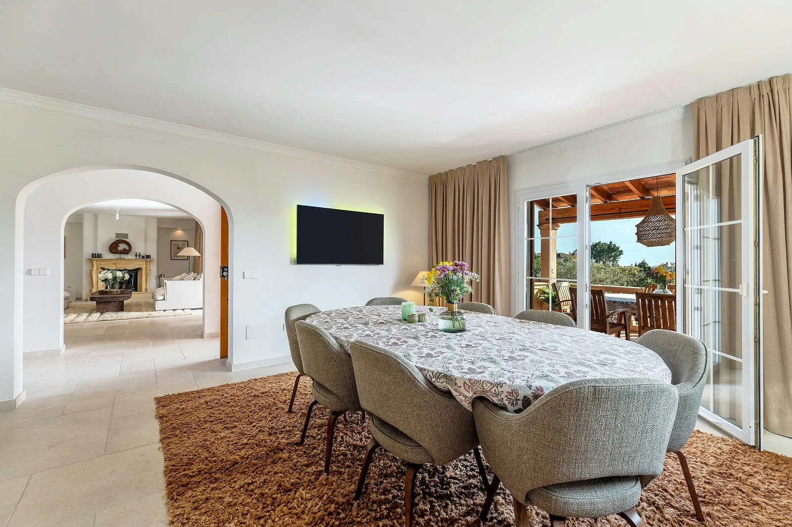Villa Scarlett dining area with oval table, comfortable chairs, shaggy rug, and archway to the main living space. Ideal luxury family rental ByMilagro.