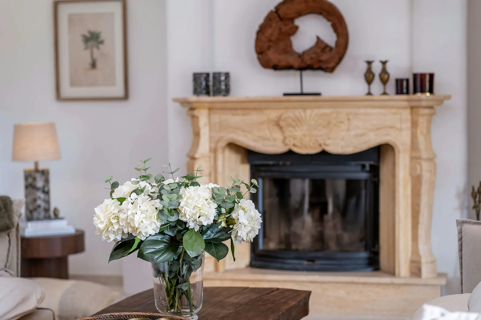 Close-up of the elegant stone fireplace and mantelpiece in the Villa Scarlett living room, decorated with flowers and art. Luxury rental ByMilagro detail.