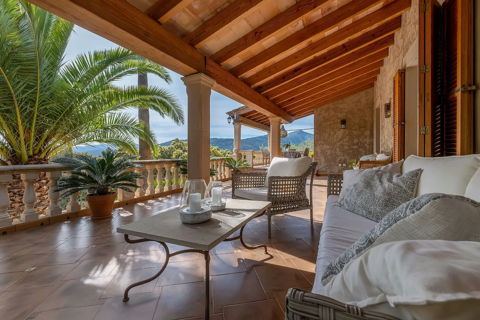 Covered terraced seating area at Villa Scarlett with cushioned wicker furniture, exposed wooden beams, and mountain views. Perfect for relaxation at ByMilagro.