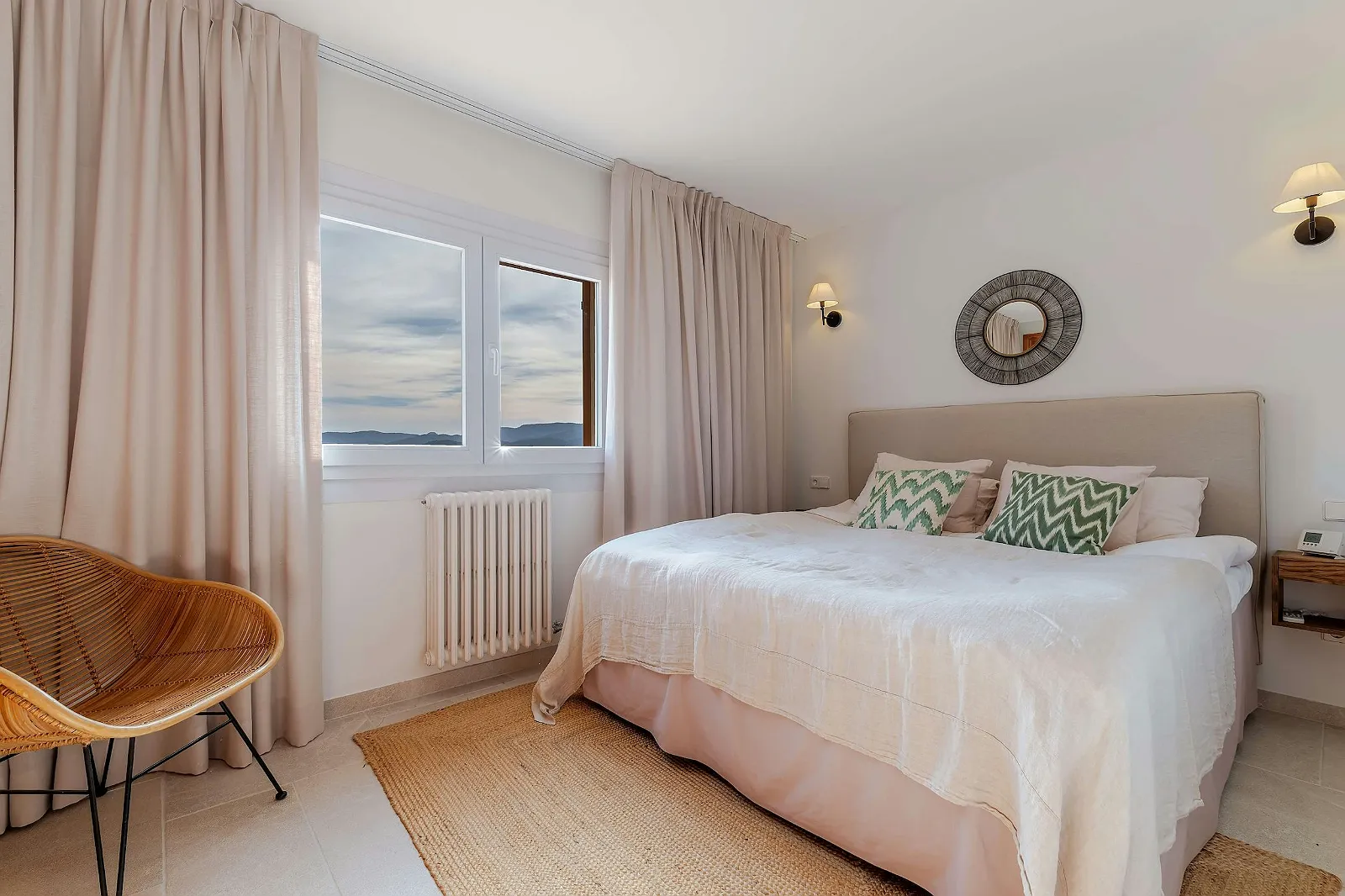 Bright bedroom in Villa Scarlett with cozy linen bed, wicker chair, mountain view window, and soft cream curtains. ByMilagro luxury accommodation.