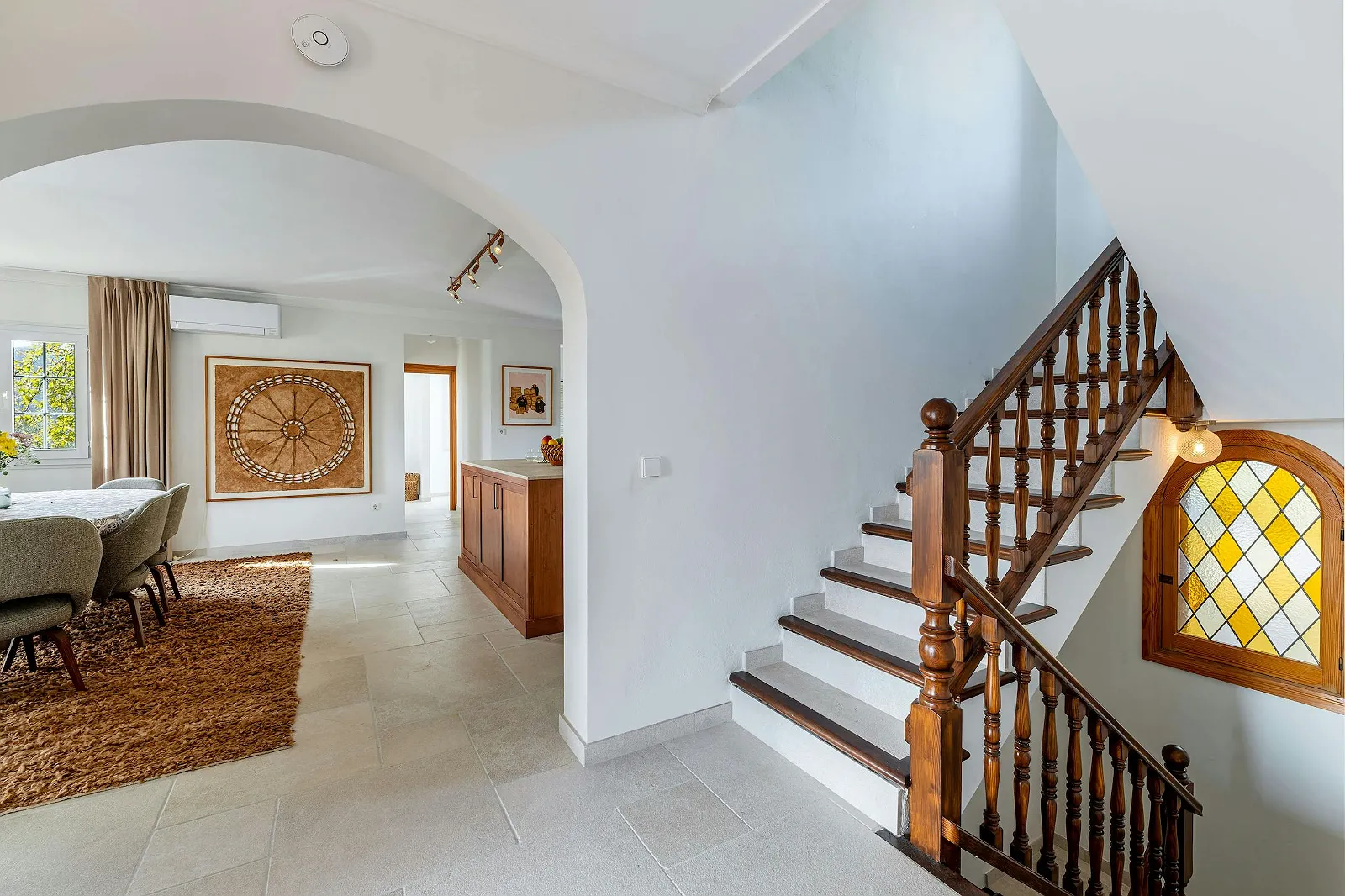 Grand entrance hall and traditional wooden staircase with a stained-glass window, connecting the dining area and upper floors of Villa Scarlett ByMilagro.