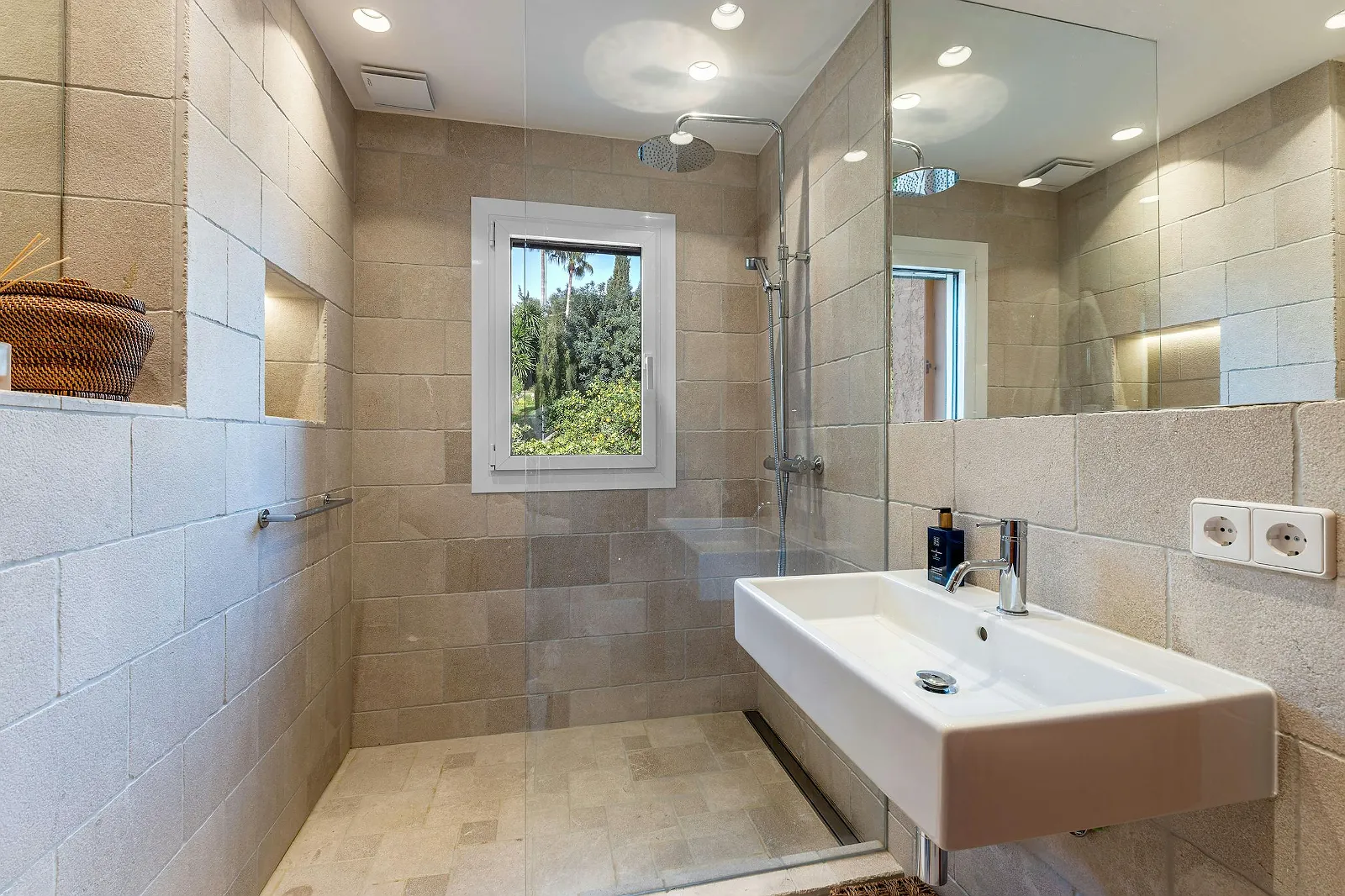 Walk-in shower area in Villa Scarlett bathroom with large neutral-colored tiles, modern fixtures, and window view. ByMilagro luxury amenities.