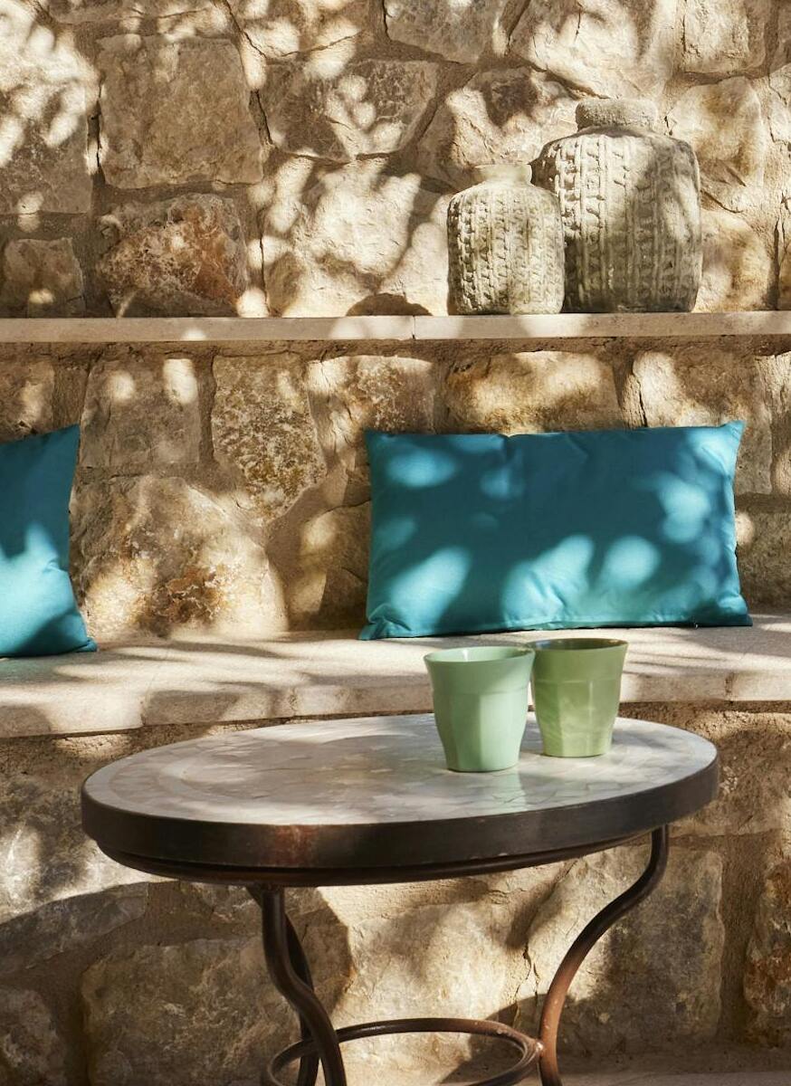 Outdoor seating niche built into a stone wall with turquoise cushions and marble accent tables. Relaxing patio at ByMilagro villa.