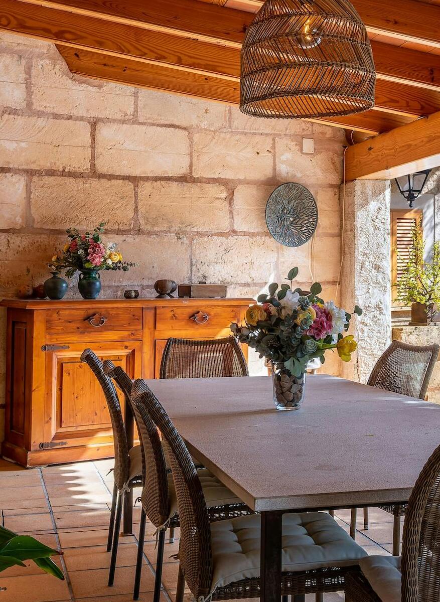 Covered outdoor dining area at Villa Scarlett with stone walls, wicker chairs, wooden sideboard, and a large dining table. Al fresco dining ByMilagro.