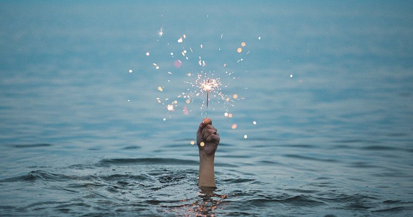 A hand holds a sparkler above water, representing hope