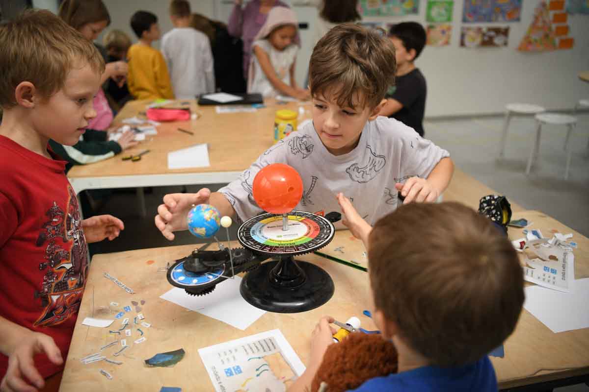 Троє молодших учнів працюють зі стендом фізичної моделі сонячної системи