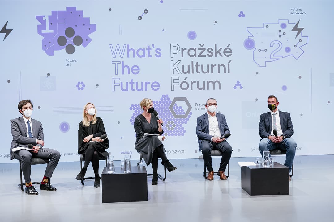 Pět panelistů s rouškami na obličeji sedí na pódiu s mikrofony během akce Pražské Kulturní Fórum s textem „What's The Future“ na pozadí obrazovky.