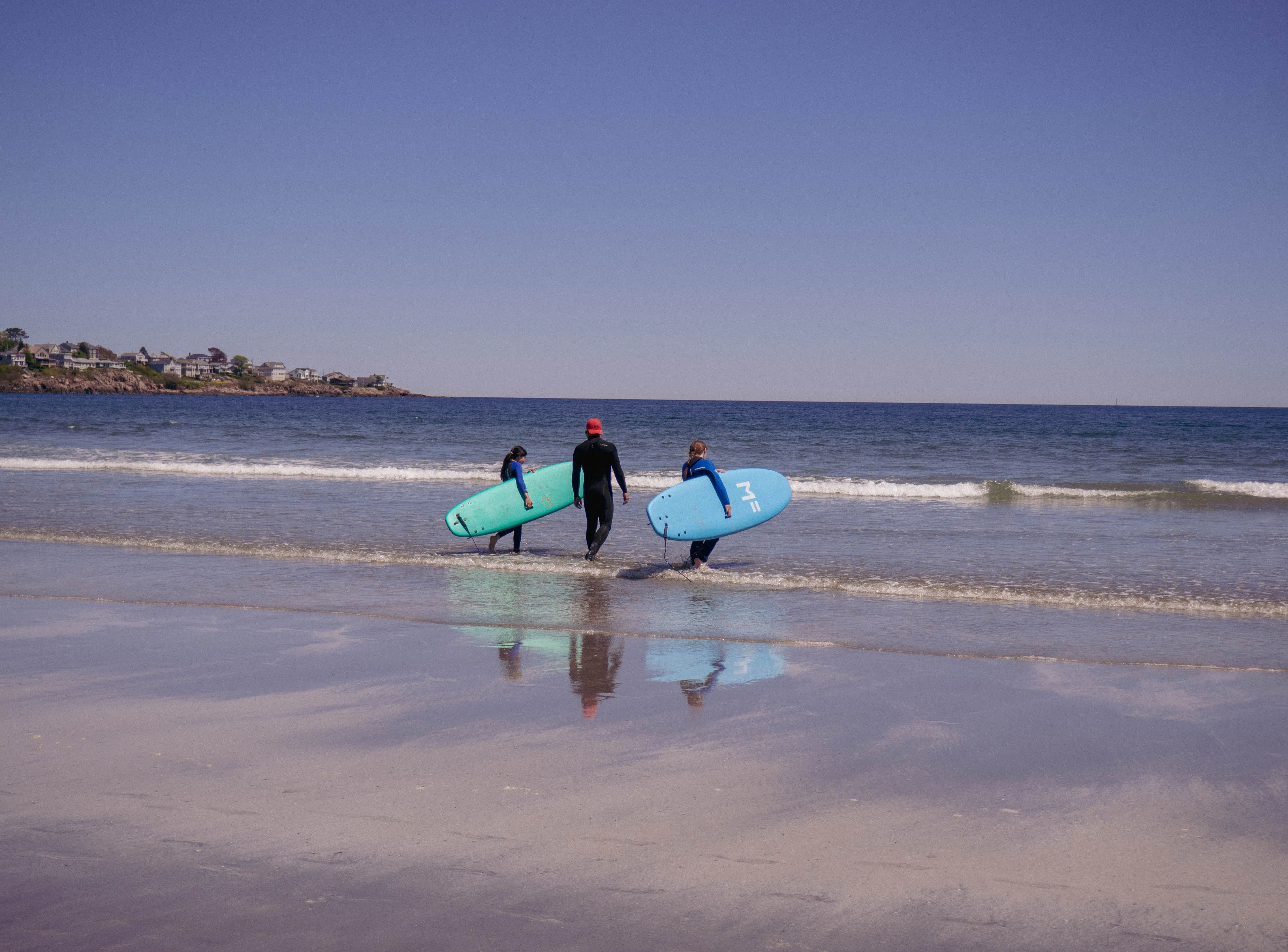 Three surfers walking on the beach with their surfboards.