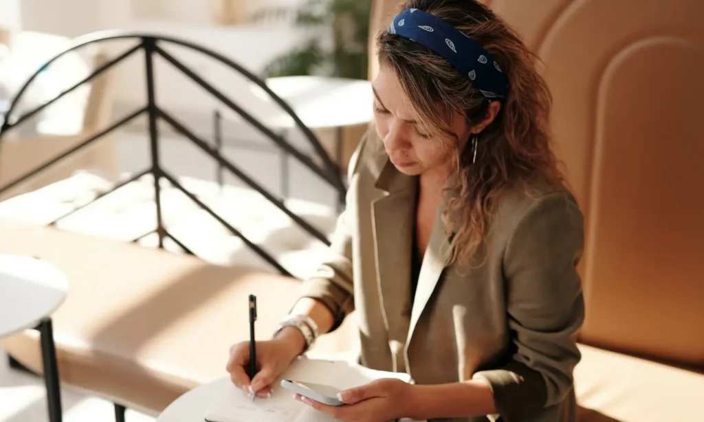 a person looking at their phone and writing in a notebook