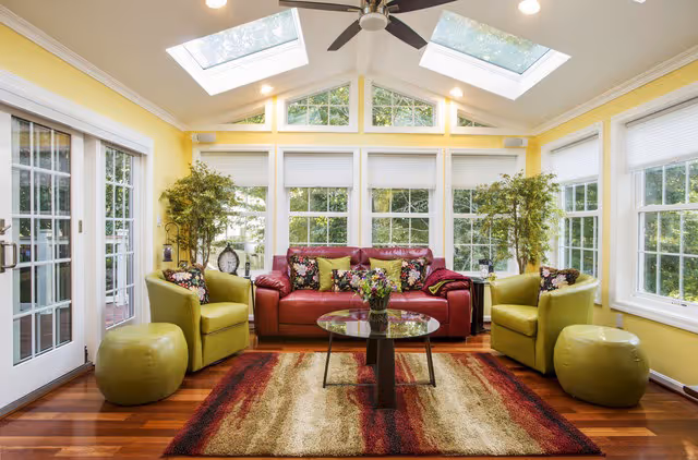 Bright sunroom construction project in Northern VA: red leather sofa, lime green chairs/ottomans, skylights, views of greenery.