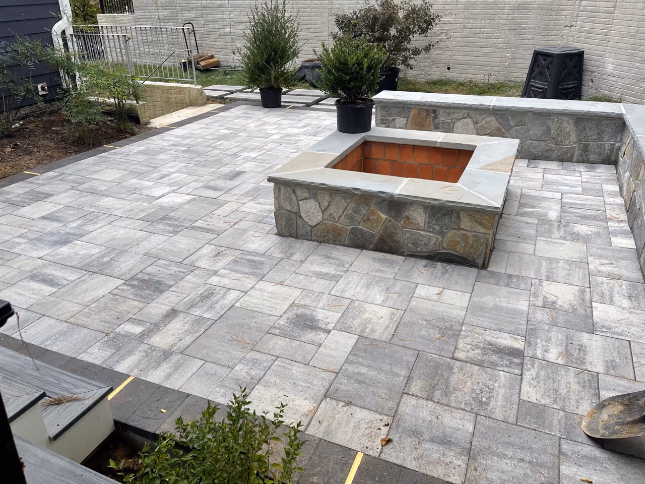 Newly constructed patio with a stone-clad fire pit and stone retaining wall.