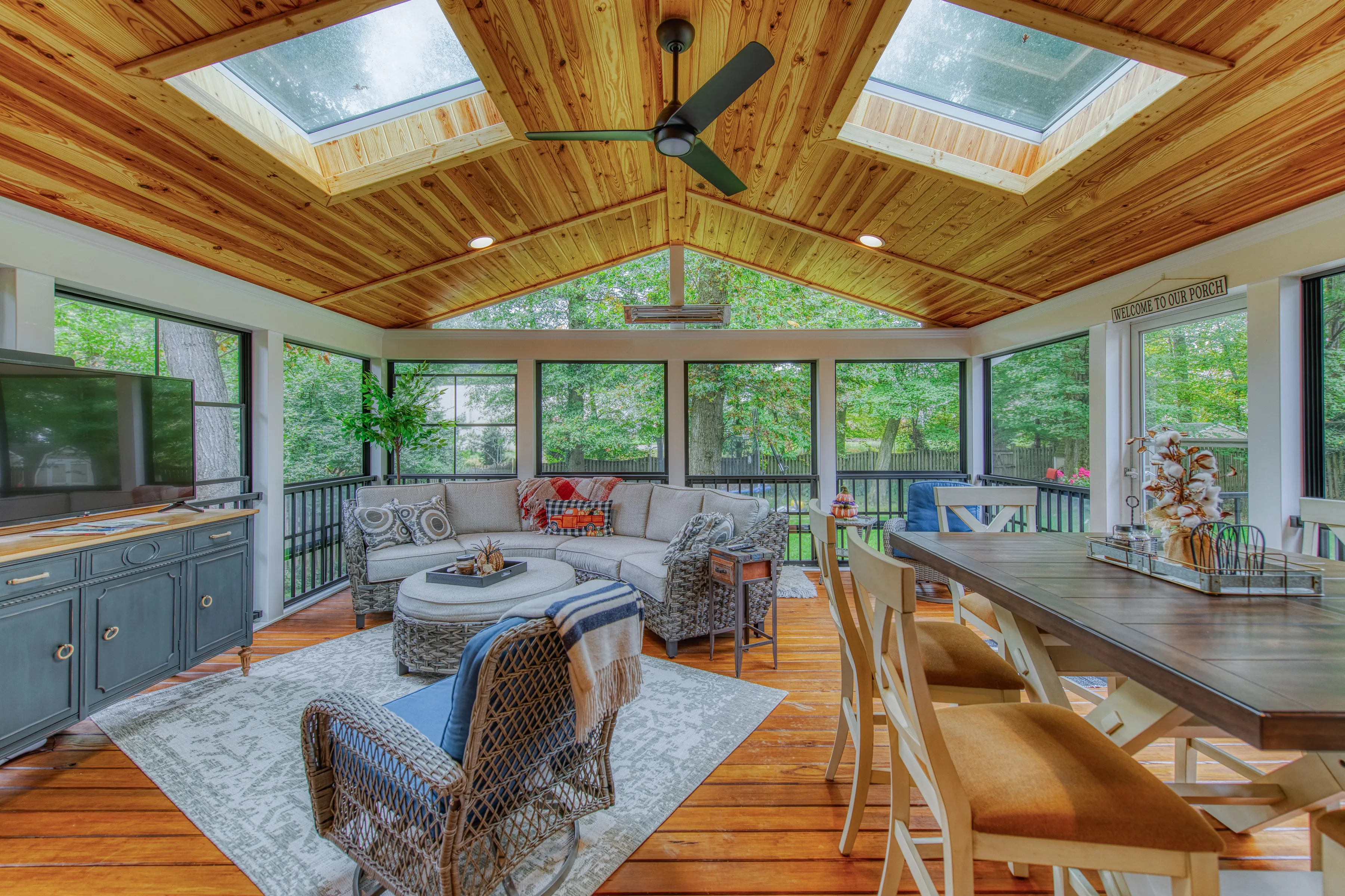 Inviting screened porch / three season room with vaulted wood ceiling, skylights, sectional sofa, and dining set overlooking greenery.