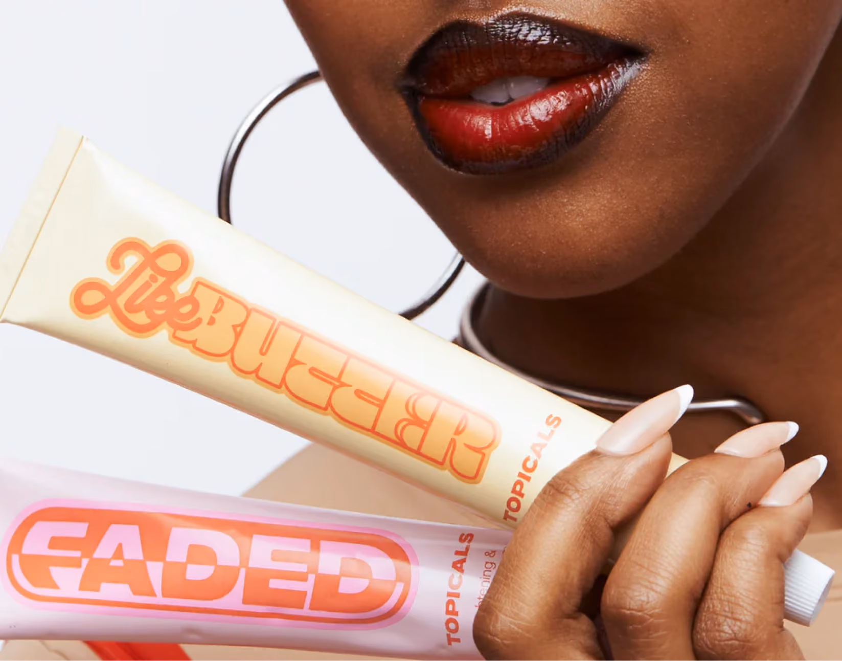 Close up of a woman holding two Topicals lip products