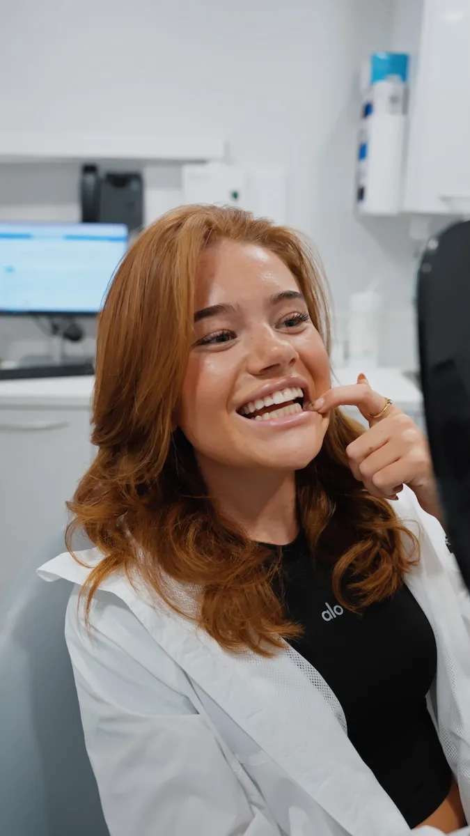 Smiling woman with red hair checking her teeth in a dental clinic chair.