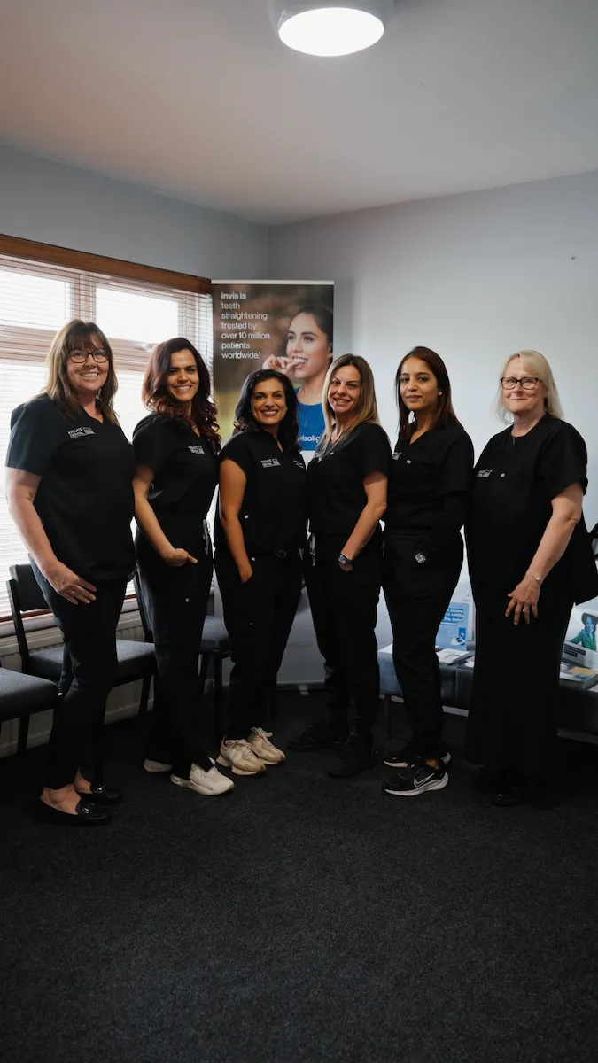 Six women in black medical uniforms standing in an office with a dental poster in the background.