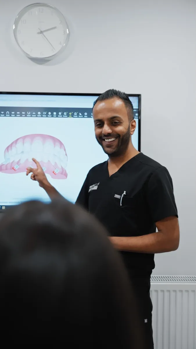 Smiling man in black scrubs points at dental image on screen in a clinical setting.