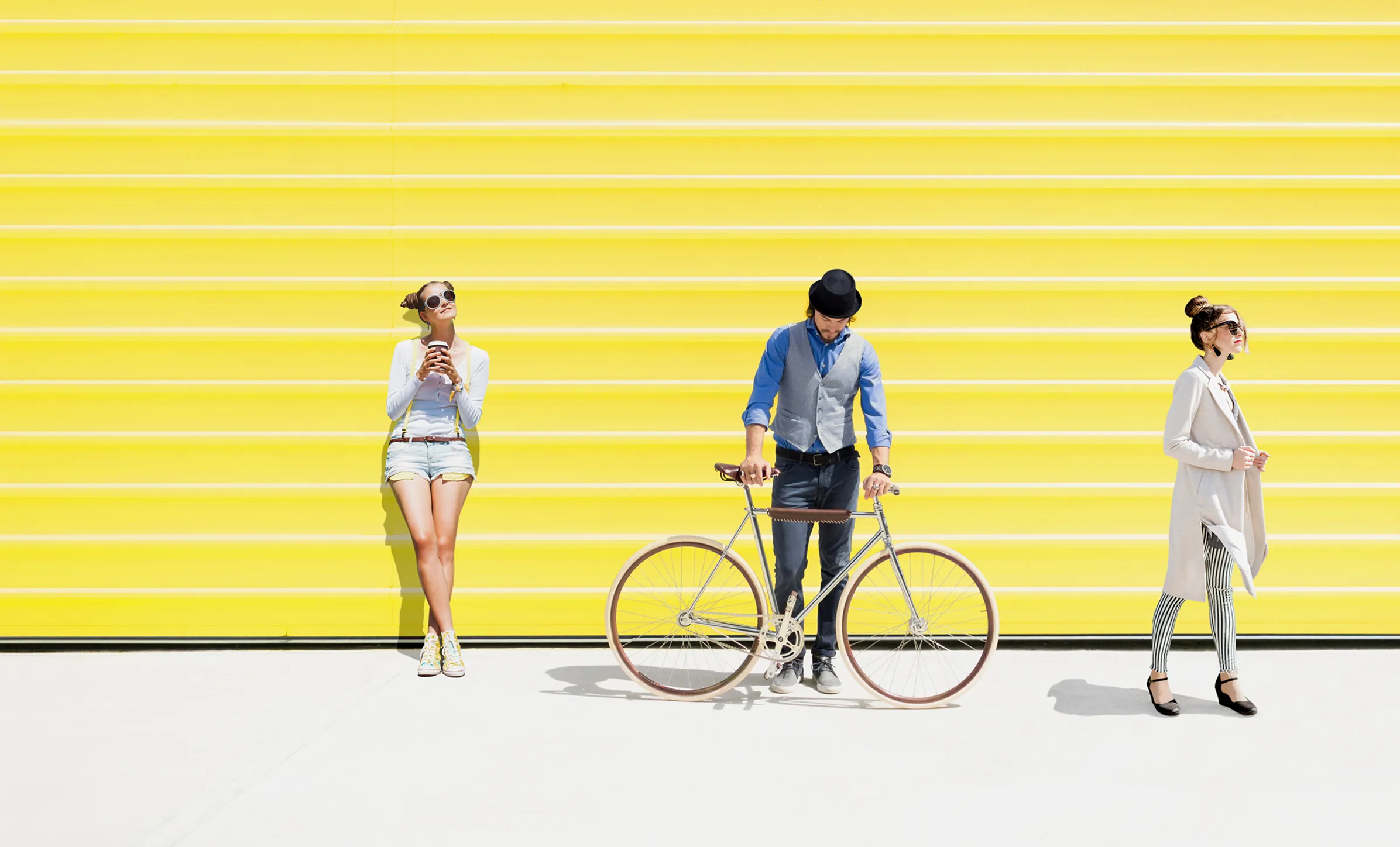 zwei Frauen und einen Mann mit einem Fahrrad vor einer gelben Wand. Yellowshark – Werbeagentur Zürich
