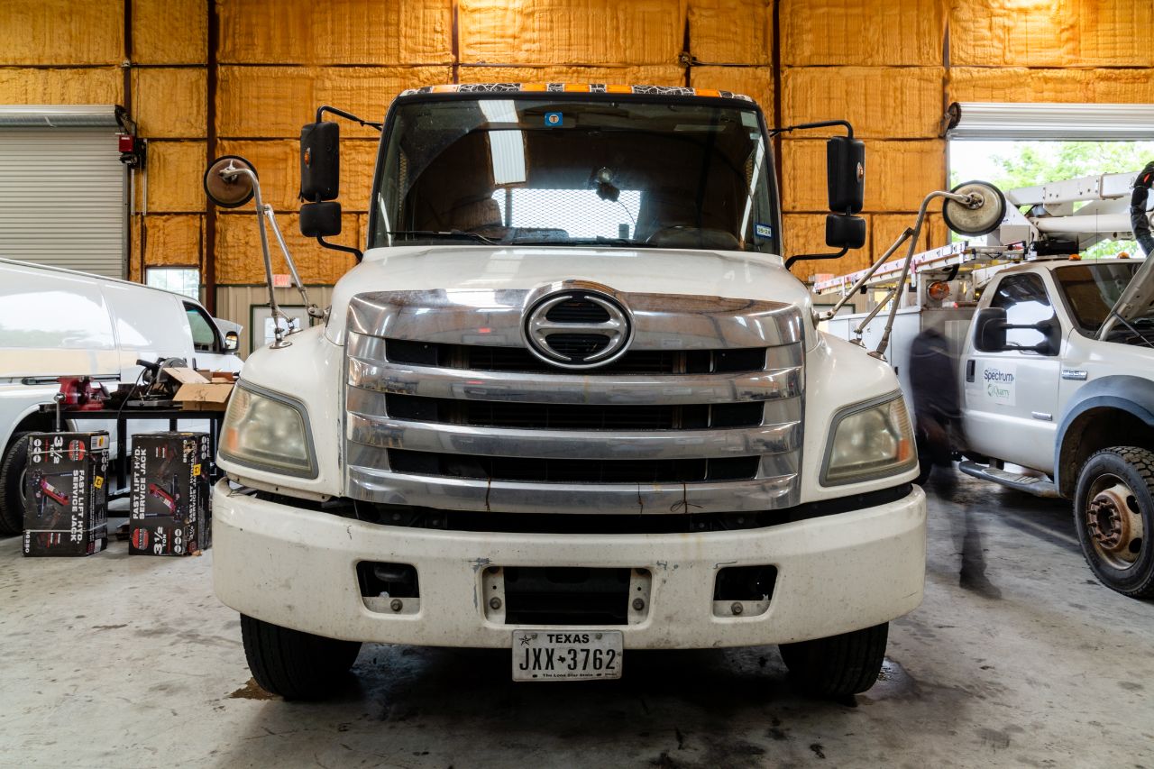 White commercial service truck with a chrome grille parked inside a fleet maintenance garage, surrounded by tools and service vehicles.