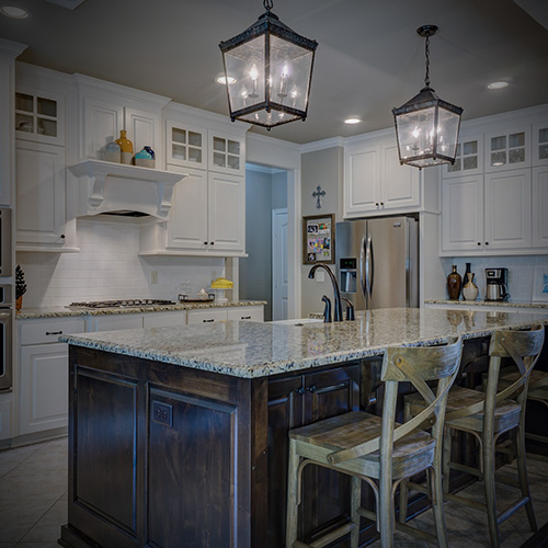 Modern kitchen with white cabinetry, granite island countertop, three wooden bar stools, and pendant lantern lights.
