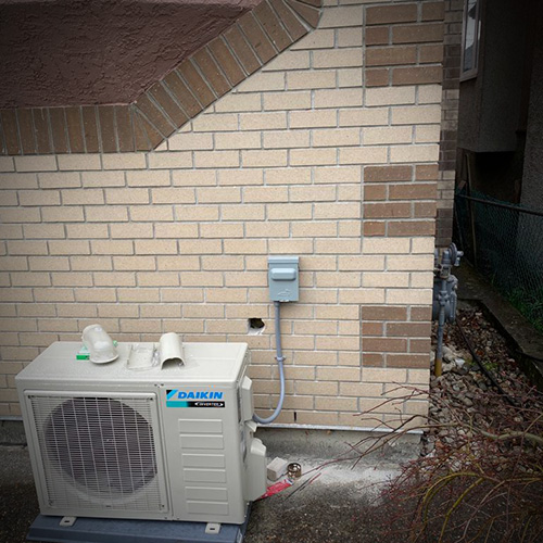 Daikin outdoor air conditioning unit installed beside a brick wall on a concrete base.